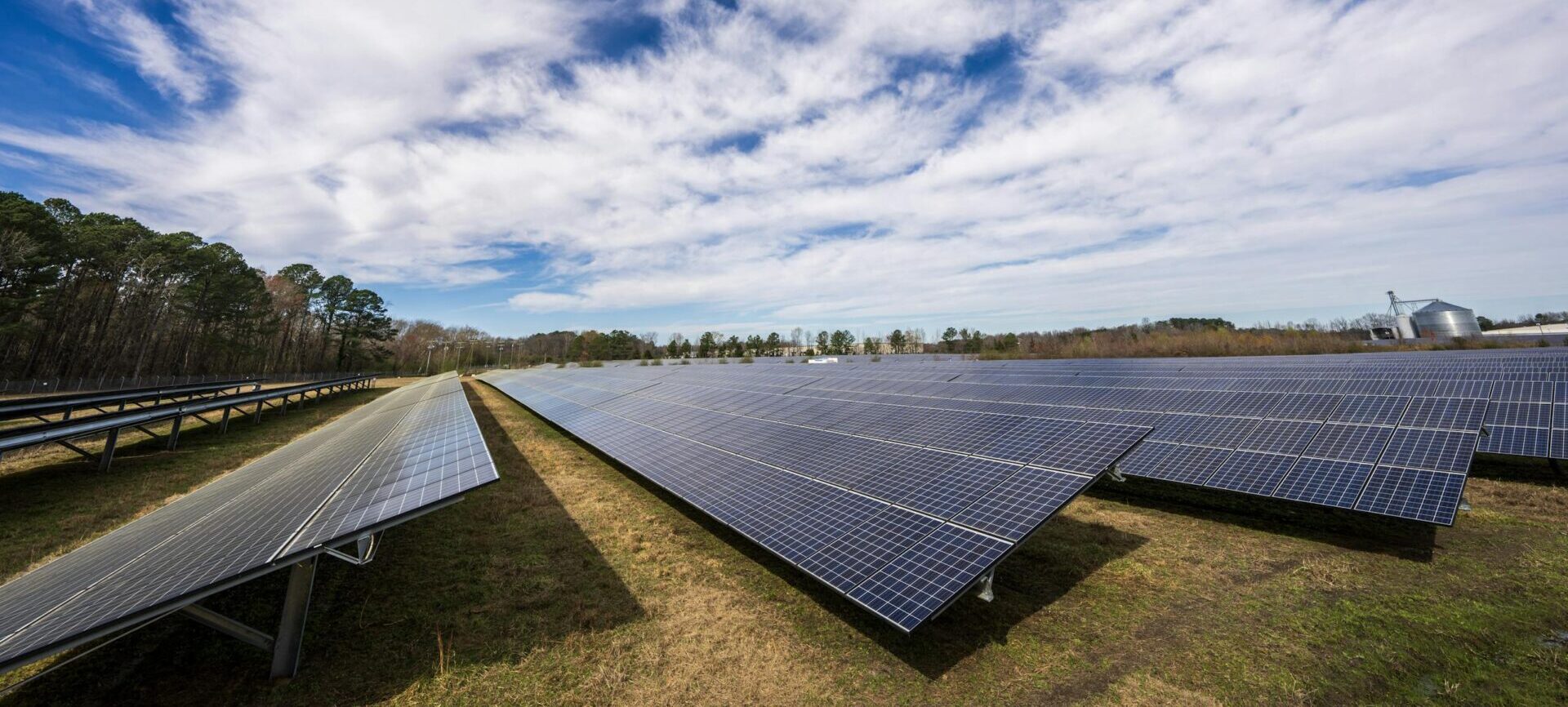 Solar panels spread across a field under a bright blue sky with clouds, showcasing renewable energy.